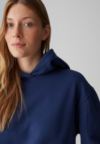 Marineblauer Hoodie mit einer Fronttasche und einer großen Kapuze. Weicher Stoff mit lockerem Sitz. Verfügt über minimale Nähte und keine sichtbaren Logos.