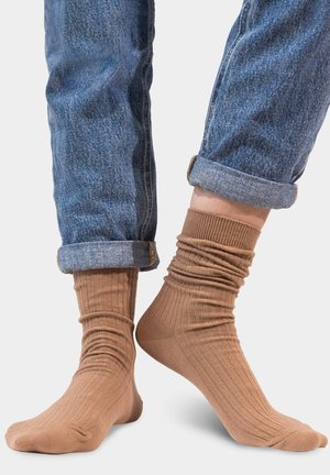 Brązowe skarpetki w prążki z teksturowanym splotem, noszone powyżej kostki, zestawione z podwiniętymi dżinsami.