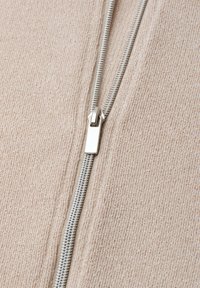Close-up of a silver zipper partially zipped on beige ribbed knit fabric.