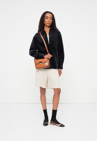 Sort corduroy oversized skjorte, cremede shorts, brun crossbody taske, sorte sokker og beige flade sko med sorte spidser. En enkel og funktionel outfitt.