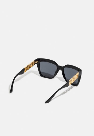 Óculos de sol pretos com uma armação retangular robusta e lentes escuras. Padrões geométricos em dourado nos ganchos criam um design distintivo.