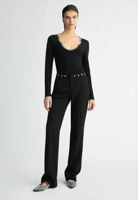 Maglietta nera a maniche lunghe con scollatura ondulata, abbinata a pantaloni neri a vita alta con cintura borchiata e ballerine nere decorate.
