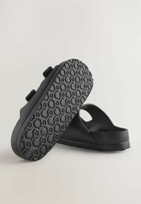 Sorte slip-on sandaler lavet af tekstureret gummi, med en honeycomb-mønstrede sål, justerbare stropper og et afrundet design med åben bag.