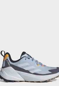 Ανοιχτό μπλε και γκρι αθλητικό παπούτσι Adidas Terrex για τρέξιμο σε μονοπάτια με λευκή σόλα, μαύρο γιακά και πορτοκαλί λεπτομέρειες στη φτέρνα και τα κορδόνια.