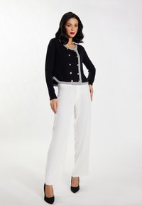 Cardigan nero cropped con bordino grigio e bottoni decorativi argentati, abbinato a pantaloni white a gamba larga e scarpe nere con tacco alto.