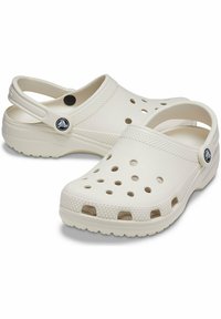 Sabots en plastique blanc avec des trous de ventilation, une sangle à l'arrière, des semelles texturées et un accent de logo circulaire sur le côté. Design à bout arrondi.