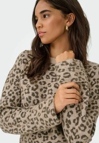 Beige sweater med mørkt leopardmønster, der har rund hals og lange ærmer. Stoffet ser blødt ud med en hyggelig tekstur.