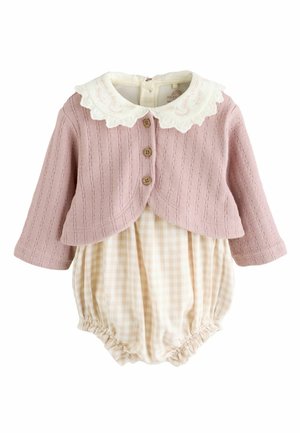Rosa gerippter Strickcardigan mit Holzknöpfen und einem weißen, gewellten Kragen über einem beigen Karo-Overall mit gerafften Beinen.