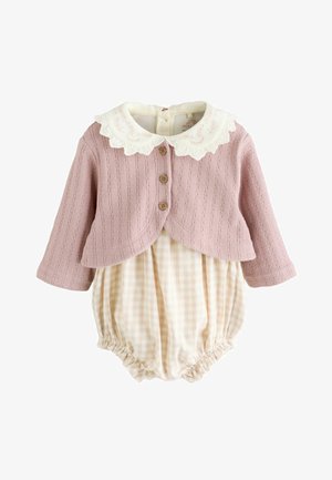 Cardigan rosa a costine con bottoni in legno e un colletto bianco a scallop sopra una salopette a quadri beige con gambe arricciate.