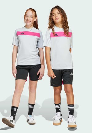 Deux enfants en t-shirts de sport gris avec des rayures roses, portant des shorts noirs et des chaussettes noires avec des rayures blanches, chaussés de chaussures Adidas.