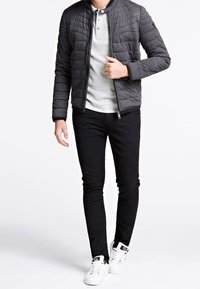 Sort quiltet jakke med rund krave, grå polo skjorte, sort slim fit jeans og hvide sneakers. Har lynlås lukning og sidelommer.