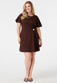 Robe brune courte en tissu doux avec une coupe décontractée, des manches courtes, un détail de nœud sur le côté et une accent décoratif en bouton doré.