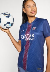 Marinsockertröjan har ett geometriskt mönster, röda och blå accenter, samt "QATAR AIRWAYS"-logotypen. Spelaren håller en fotboll.