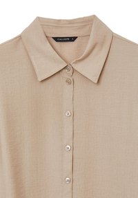 Camicia beige con bottoni, dal collo classico e tessuto testurizzato, con cinque bottoni visibili sulla parte anteriore centrale.