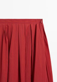 Jupe plissée rouge avec une texture lisse, dotée d'une fermeture éclair latérale et d'une large taille pour un design structuré.