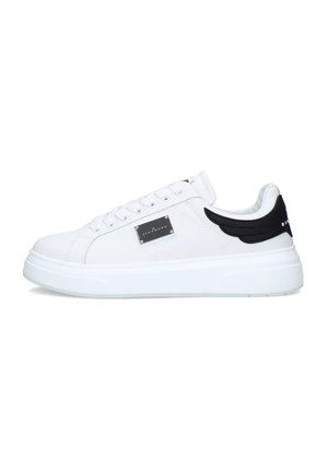 Sneaker bianca modello low-top con suola spessa, dettaglio nero sul tallone a forma di ali, piastra laterale in metallo e lacci bianchi su sfondo bianco.