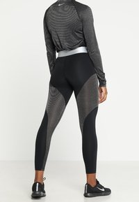 Maglietta sportiva nera a maniche lunghe e leggings presentano un design testurizzato con pannelli in mesh. La vita è di colore argento e le scarpe hanno un motivo nero e argento.