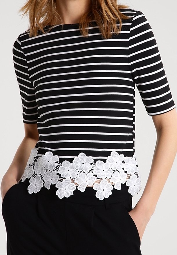 Mustassa ja valkoisessa raidallisessa t-paidassa on lyhyet hihat, ja siinä on valkoinen pitsikoristeinen helma. Pehmeä materiaali, vartalonmyötäinen muotoilu ja pyöreä pääntie.