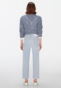 Modrý pletený svetr s texturovaným vzorem, kombinovaný s bledě modrými džíny rovného střihu. Bílé nazouvací boty dotvářejí outfit.