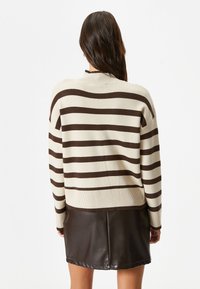 Dzianinowy sweter w kolorze kremowym z brązowymi poziomymi paskami, luźny krój, ściągacze przy mankietach i u dołu, noszony na czarną skórzaną spódnicę.