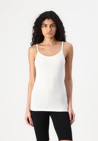 Top en coton blanc à fines bretelles, col rond et silhouette ajustée, associé à un short noir. Texture douce, design minimaliste.