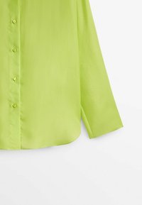 Chemise boutonnée à manches longues vert citron vif avec une texture de tissu lisse, montrée de la section médiane jusqu'à la manche sur un fond blanc.