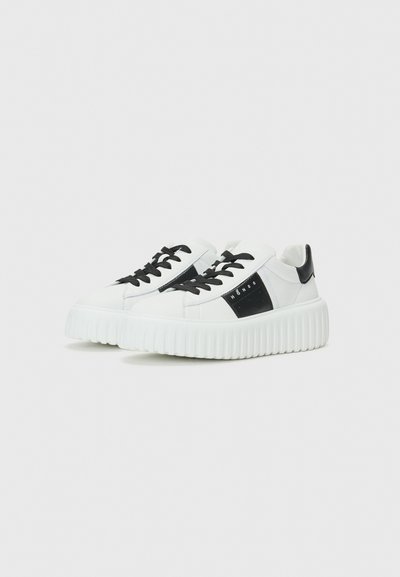 Baskets blanches avec une semelle en caoutchouc texturée, des lacets noirs et un panneau d'accent noir. Tige supérieure lisse en synthétique avec un design géométrique.
