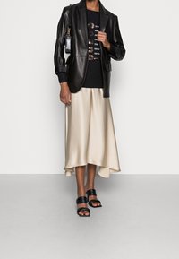 Schwarze Lederblazer, schwarzes Grafik-T-Shirt, cremefarbene Satinröhre mit asymmetrischem Saum und schwarze Riemchensandalen.