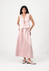 Roosa kihiline top, millel on volangservad, koos pika satiinist roosa seelikuga. Kingad on heleda roosa värvi ja rihma kujundusega. Lihtne, elegantne stiil.