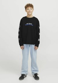 Sudadera negra de manga larga con texto azul, que presenta gráficos de estrellas y círculos blancos. Combinada con jeans de un azul claro y zapatos negros.