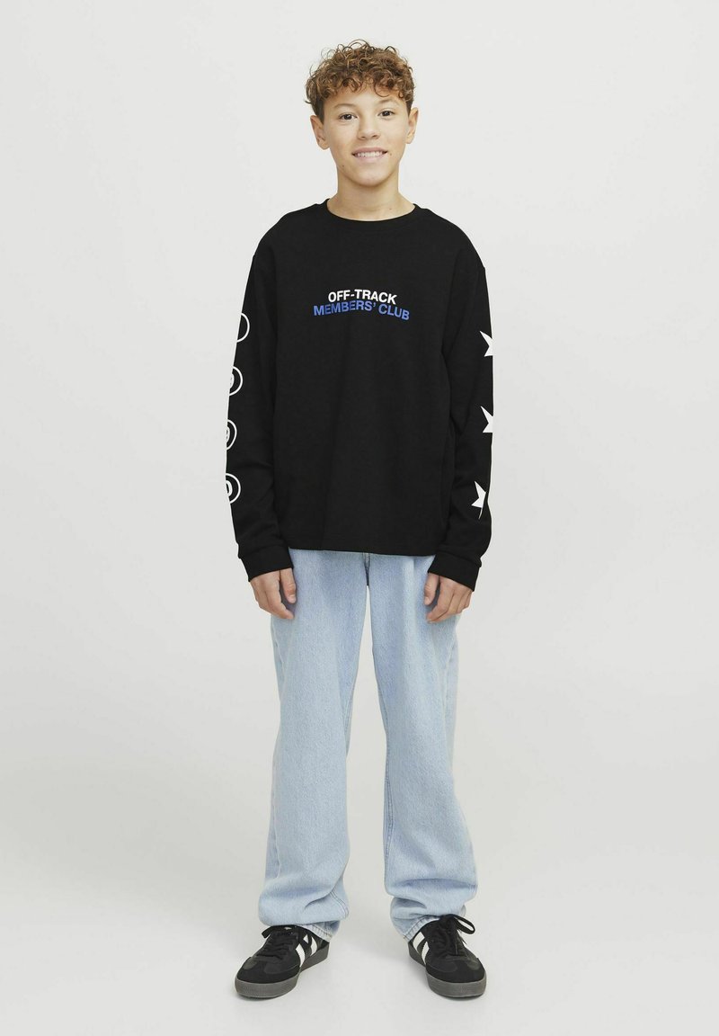 Sudadera negra de manga larga con texto azul, que presenta gráficos de estrellas y círculos blancos. Combinada con jeans de un azul claro y zapatos negros.