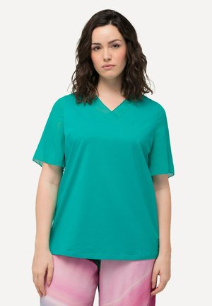 Top a maniche corte e scollo a V in tessuto teal, con una vestibilità morbida e una texture liscia. Indossato con pantaloni rosa a fantasia.