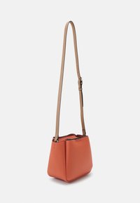 Mała strukturalna torebka crossbody w kolorze przypalanej pomarańczy, wykonana ze skóry, z jaśniejszym, regulowanym paskiem oraz czarnym suwakiem na górze, prezentowana na białym tle.