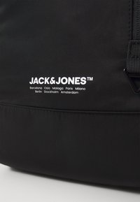 Czarna torba z materiału z logo "JACK & JONES" w białym kolorze, z nazwami miast nadrukowanymi poniżej. Gładka tekstura, minimalistyczny design i solidne akcesoria.