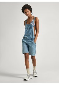 Denim ülerõngad helesinises värvitoonis, lühikese pikkusega, reguleeritavate rihmadega, esikotiga ja mugava lõikega. Kandmine triibulise bikiiniga.