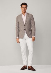 Blazer en pied-de-poule marron clair avec deux poches avant, associé à une chemise rayée rose et un pantalon blanc. Des mocassins en cuir marron viennent compléter le look.