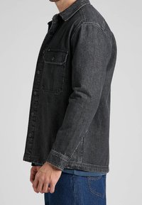 Černá džínová bunda s límečkem, předním zapínáním na knoflíky a náprsní kapsou. Tkanina má texturovaný vzhled s mírně vybledlým efektem.