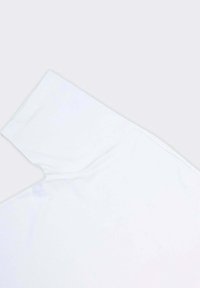 T-shirt bianco a maniche corte con scollatura rotonda e texture morbida, esposto in un angolo su uno sfondo semplice.