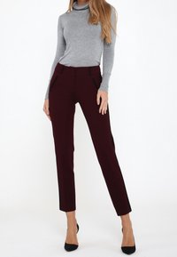 Pantalons slim-fit bordeaux avec accents noirs sur les côtés et poches, associés à un haut en col roulé gris. Tissu lisse, design ajusté.