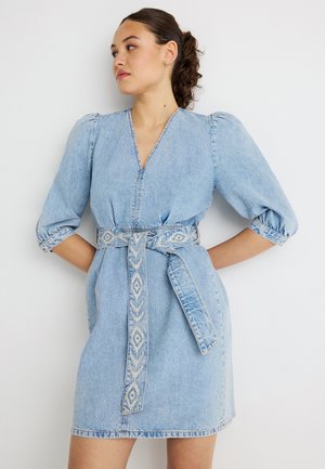 Vestido de mezclilla en azul claro con mangas abullonadas, escote en V y cinturón bordado en la cintura con patrones geométricos. Tela suave y texturizada.