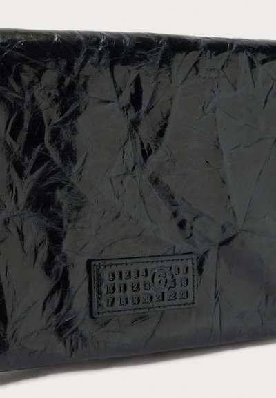 Γυαλιστερή μαύρη επιφάνεια από δερματίνη με ραμμένη ορθογώνια ετικέτα που δείχνει αριθμούς από το 0 έως το 23 και έναν αριθμό 6 μέσα σε κύκλο.