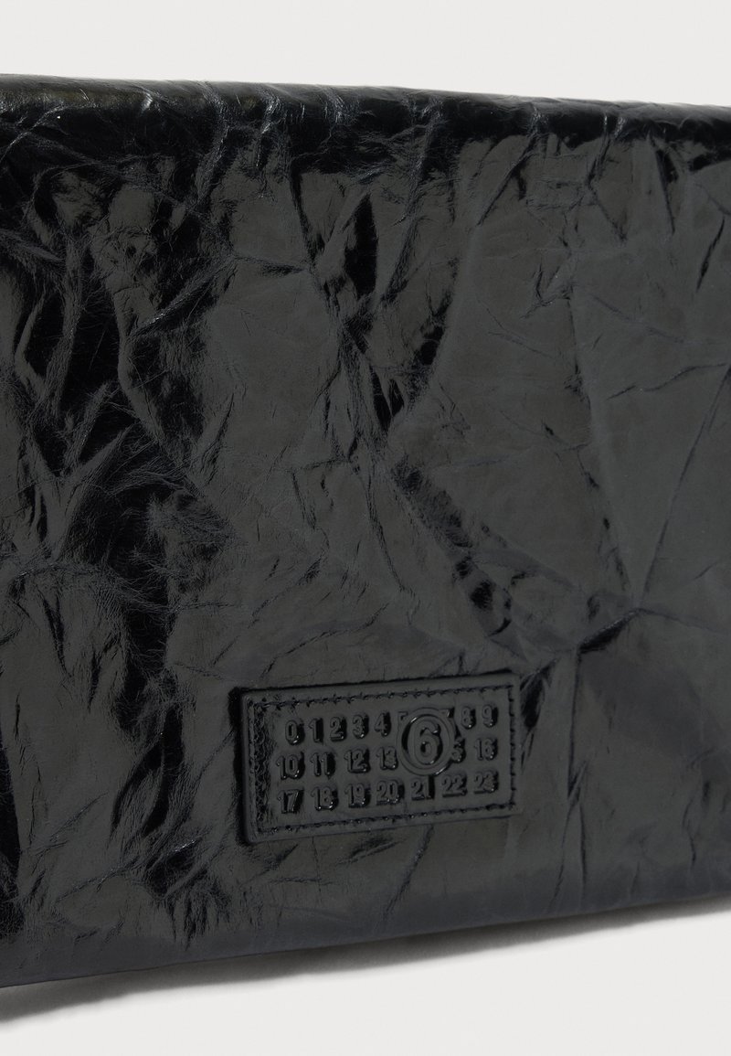 Glansfuld sort læderoverflade med tekstur og en syet rektangulær etiket, der viser numrene 0 til 23 samt et indrammet nummer 6.