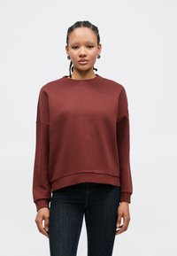 Bordeauxrød sweatshirt i blødt stof med rund halsudskæring, sænkede skuldre og ribstrikkede manchetter. Kombineret med mørke jeans.