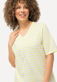 Camiseta de rayas de algodón suave con rayas horizontales amarillas y blancas, diseño de escote en V y un gráfico en gris claro en la parte frontal.