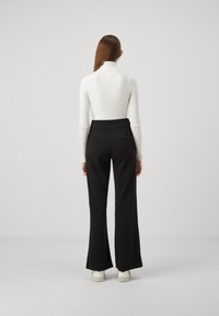 Hvit ribbestrikket turtleneck topp kombinert med høy midje svarte flagrende bukser; vist fra baksiden, med hvite sneakers synlige.