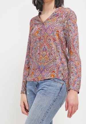 Blusa paisley multicolore con maniche lunghe e scollatura a V, caratterizzata da motivi intricati in viola, arancione e blu, abbinata a jeans blu.