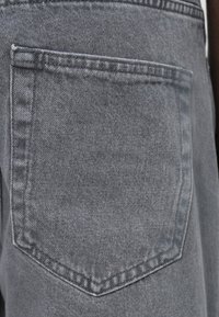 Jeans in denim grigio con una tasca sul retro a forma rettangolare, caratterizzati da cuciture rinforzate e una finitura in tessuto liscia e testurizzata.