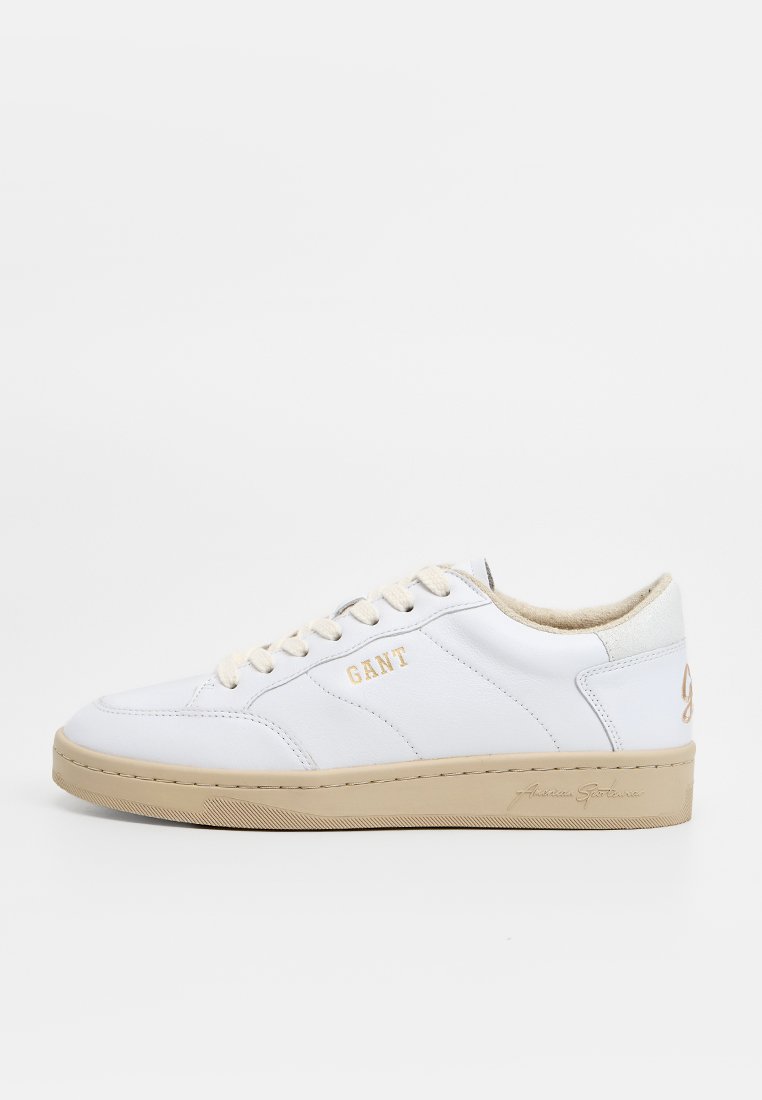Zapatilla de piel blanca con suela de goma beige, que presenta un logo dorado de "GANT" y suaves acentos texturizados en el talón y la lengüeta.