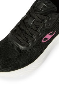 Zapatilla deportiva de malla negra con cordones negros, suela blanca y logo rosa en el lateral.