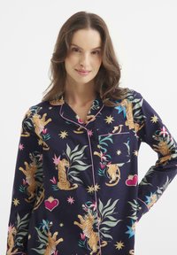 Pigiama top blu navy con un motivo di tigri e piante in colori vivaci. Materiale in cotone, con piping rosa e taschino sul petto.